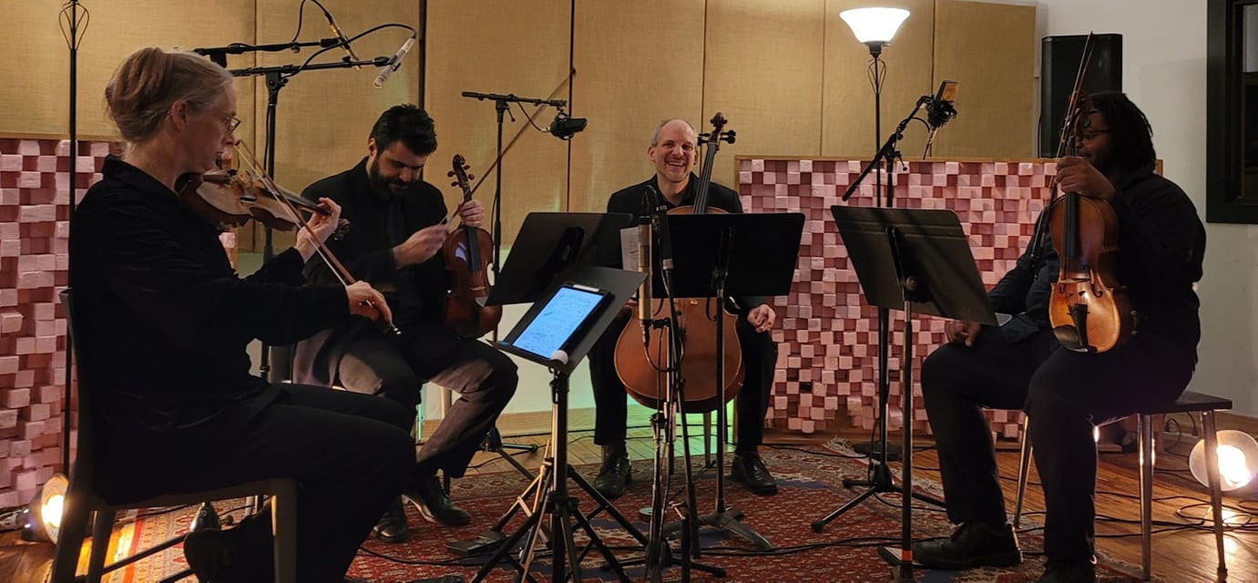 The Crossing Borders Music string quartet warm up their instruments and joke around before a program. Photo credit Mike King