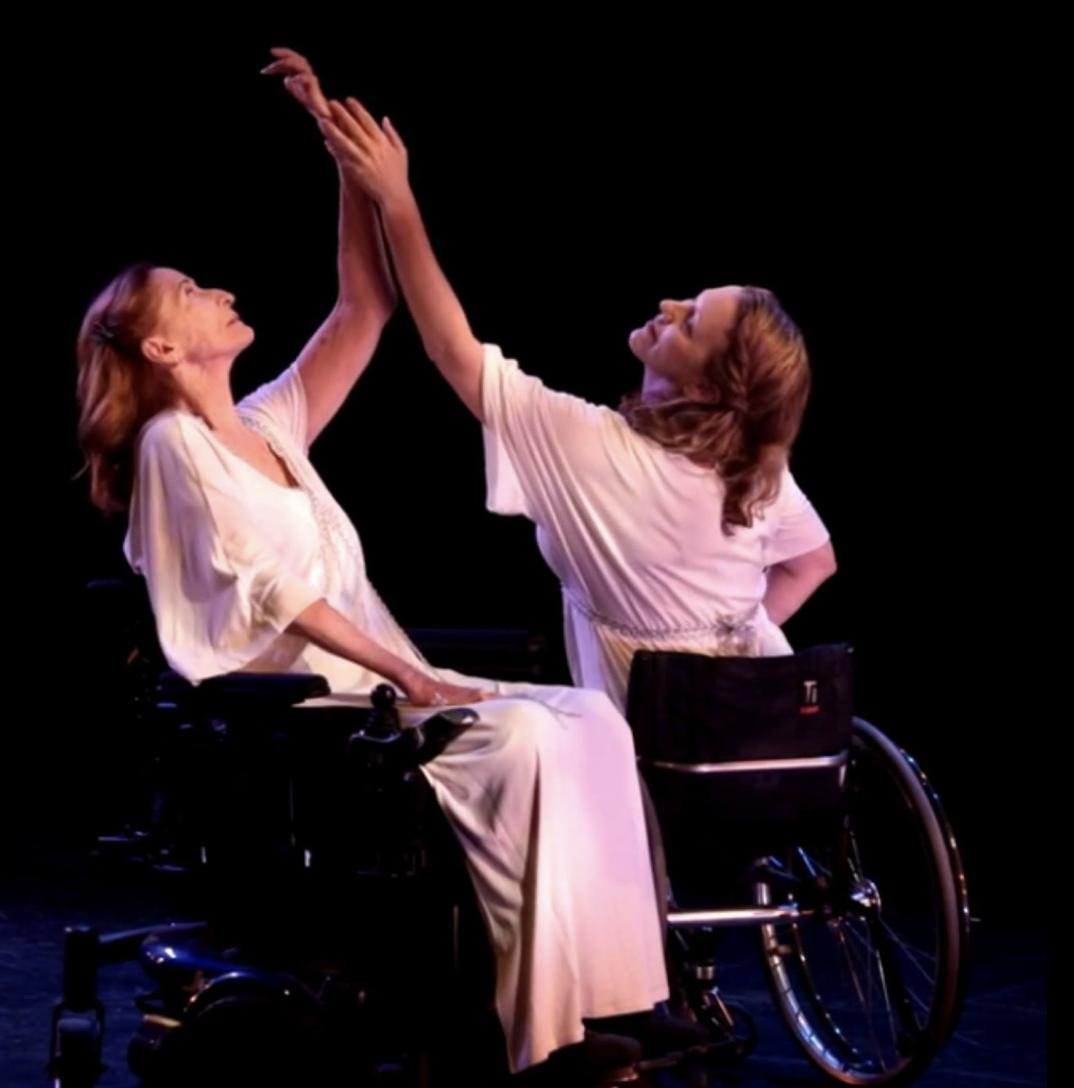Momenta Dance Company's Facebook profile picture of two women wearing flowing white dresses, both in wheelchairs, facing one another with arms gracefully lifted.